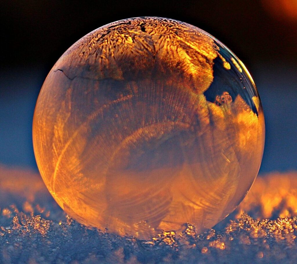 Close-up shot of a frozen bubble with warm reflections resting on a snowy surface at twilight.