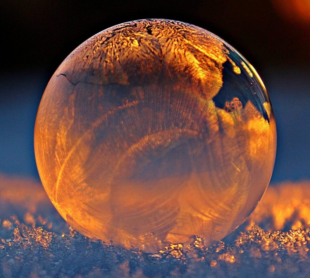 Close-up shot of a frozen bubble with warm reflections resting on a snowy surface at twilight.